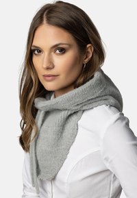 Lys grå strikket tørklæde med et oversized design, der har en blød tekstur og justerbare bånd, båret over en hvid skjorte.