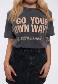 Gray cotton t-shirt with loose fit, featuring large peach text "GO YOUR OWN WAY" and "Fleetwood Mac" in a smaller font below.