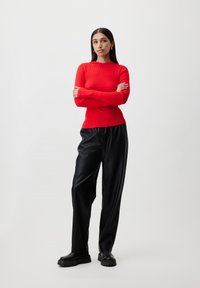 Red ribbed long-sleeve top paired with loose black faux leather pants and black chunky-soled boots, featuring a smooth texture and fitted design.