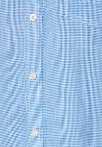 Tela de camisa a cuadros azules con una pequeña tapeta de botones, textura suave y un bolsillo en el pecho. Predominantemente de color azul claro con acentos más oscuros.