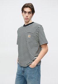 Μπλούζα με ασπρόμαυρες ρίγες, στρογγυλή λαιμόκοψη, κοντά μανίκια και τσέπη στο στήθος με λογότυπο. Συνδυάζεται με ανοιχτόχρωμο μπλε τζιν.