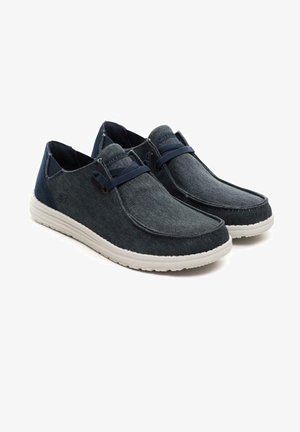 Zapatos slip-on de denim de color azul oscuro, con suela de goma blanca, acentos en contraste y detalles de cordones para un ajuste seguro.