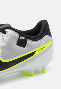 Bottines de football Nike Tiempo avec une tige en cuir gris, des accents noirs, des détails jaunes néon et une surface texturée pour l'adhérence.
