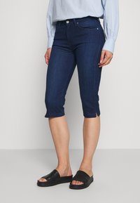 Tummansinisiä denim-capri farkkuja, joissa on kapea istuvuus, edessä nappisuljenta, taskut ja lyhennetty helma sivuhaalareilla.