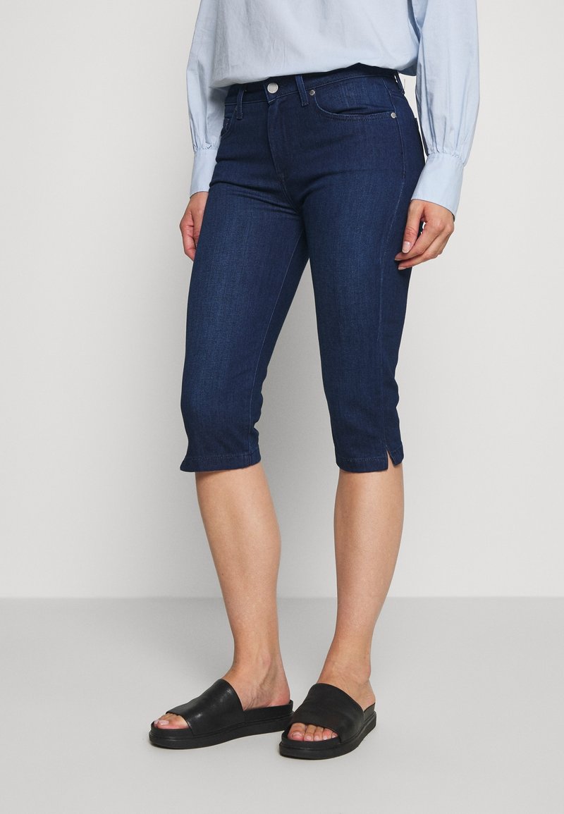 Tummansinisiä denim-capri farkkuja, joissa on kapea istuvuus, edessä nappisuljenta, taskut ja lyhennetty helma sivuhaalareilla.