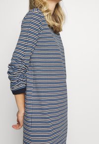 Robe à manches longues à motifs bleu marine et bleu clair, coupe décontractée, avec poignets côtelés et tissu texturé. Col en V, fentes latérales.