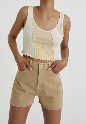 Top en crop en crème et jaune pastel avec des bords festonnés, associé à un short taille haute beige avec des bords effilochés et des poches avant.
