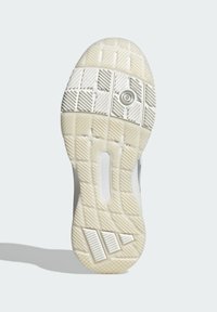 Podeszwa buta z teksturowaną, białą gumową powierzchnią, z różnymi wzorami bieżnika i wyraźnym detalem logo na pięcie.