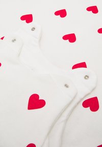 White fabric garment featuring a pattern of red hearts, with snap fasteners at the shoulder for closure and a soft texture.