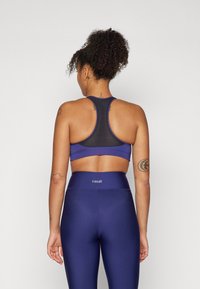 Marineblå sports-bh med mesh-back, kombinert med høyt midjes leggings med logo på midjen. Glatt tekstur og tettsittende design.