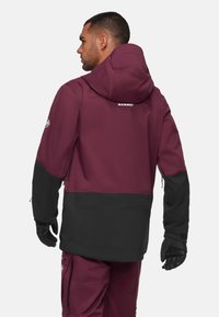 Bordeauxrote und schwarze wasserdichte Jacke mit Kapuze, die ein schlankes Design, strukturierten Stoff und eine mit Reißverschluss verschlossene Tasche am Arm bietet.