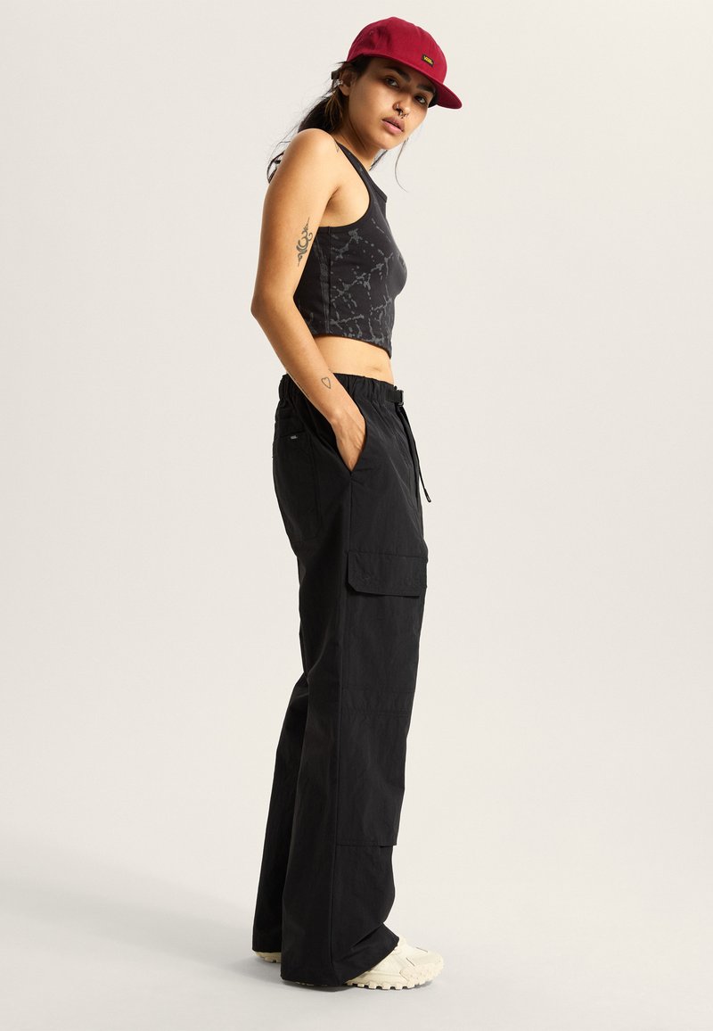Pantalones cargo negros con bolsillos laterales, cintura elástica y un ajuste holgado. Combinados con un top corto negro con estampado y una gorra burdeos.