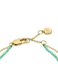 Guldspänne med kort förlängningskedja och hjärtformat märke på ett halsband som kombinerar guldkedjor och små gröna pärlor.