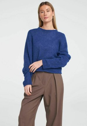Blue wool blend sweater with a round neckline and long sleeves, paired with loose brown trousers. Textured knit adds depth to the design.