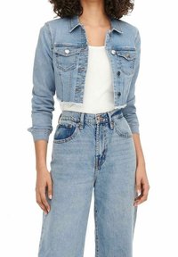 Mujer vistiendo una chaqueta de mezclilla azul claro cortada sobre una blusa blanca y unos jeans de mezclilla de tiro alto y corte holgado.