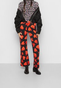 Svarta byxor med röda hjärtan, kombinerat med en åtsittande, mönstrad topp och en svart bomberjacka. Solida svarta stövlar fulländar looken.