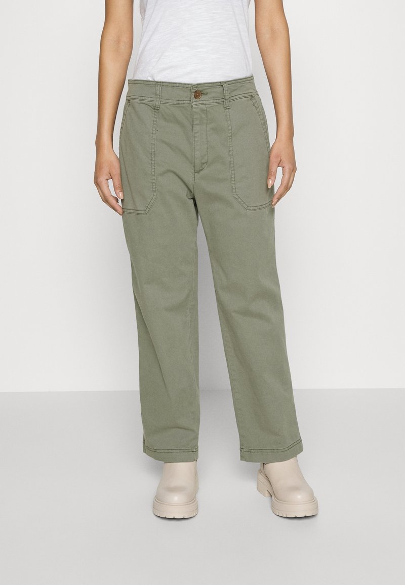 Ljusgröna vida byxor med framfickor, en knappstängning och synlig sömnad. Kombination med neutrala ankelboots.