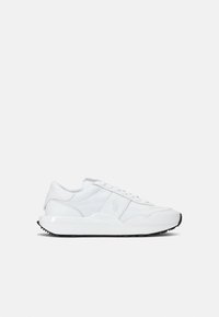 Baskets de sport blanches avec une tige en cuir lisse, des accents texturés, des lacets plats et une semelle en caoutchouc noire. Logo affiché sur le côté.