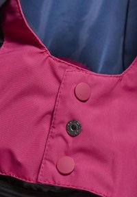 Pink fabric with a smooth texture featuring two round buttons, one red and one black, located near a dark interior lining.