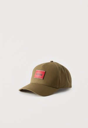 Casquette de baseball vert olive avec une visière incurvée et un patch rectangulaire rouge portant l'inscription "HUGO" au centre avant.