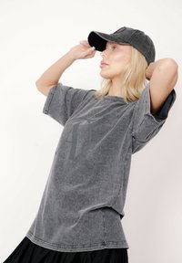 Szary, oversize'owy t-shirt wykonany z miękkiej tkaniny z lekko postarzanym wykończeniem i dużym ciemnym nadrukiem na przodzie. Połączony z szarą czapką.