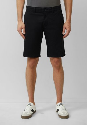 Schwarze Denim-Shorts mit geradem Schnitt, vorderem Knopfverschluss und Seitentaschen. Tragen mit weißen Sneakers mit schwarzen Akzenten.