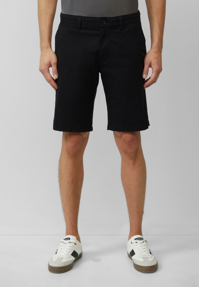 Zwarte denim shorts met een rechte snit, een sluiting met een knoop aan de voorkant en zijzakken. Gecombineerd met witte sneakers met zwarte accenten.