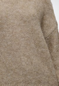 Gros plan sur un tissu tricoté beige doux avec une surface texturée et duveteuse et un motif de tricot simple.
