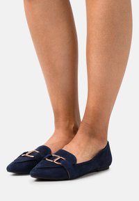 Ballerine in suede blu navy con punta affusolata, dotate di una fibbia dorata sul davanti e suola piatta in gomma.