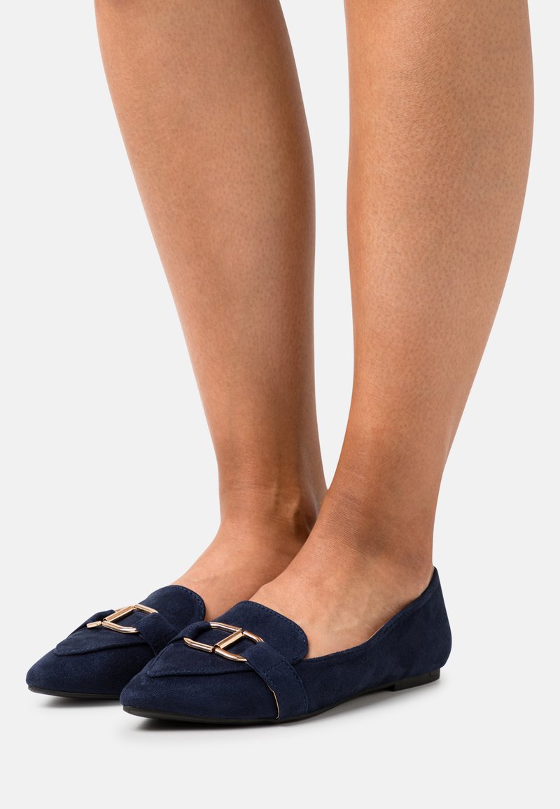 Ballerine in suede blu navy con punta affusolata, dotate di una fibbia dorata sul davanti e suola piatta in gomma.