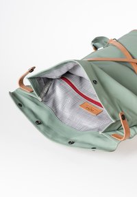 Borsa verde impermeabile con accenti in pelle marrone. L'interno presenta un motivo a griglia grigia e una tasca con zip rossa. Parte superiore aperta con chiusure a scatto.