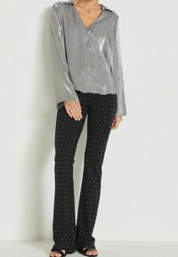 Silver, long-sleeve blouse with a V-neck and front buttons, paired with black, flared pants adorned with white dots and side slits.