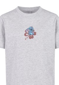 Grå bomulds t-shirt med et lille grafisk billede af en blå karakter, der sidder på en pink blomst med en struktureret baggrund.