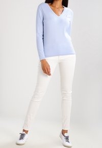 Maglione azzurro chiaro a scollo a V in tessuto morbido, abbinato a pantaloni bianchi slim-fit e sneakers bianche, creando un look casual.