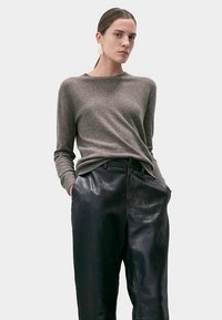 Szary dzianinowy sweter z okrągłym dekoltem, zestawiony z czarnymi skórzanymi spodniami z wysokim stanem o błyszczącym wykończeniu.