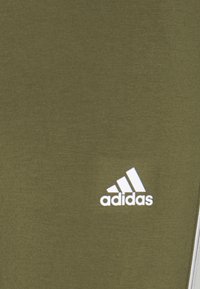 Oliivivärinen kangas, jossa on sileä rakenne. Alavasemmassa kulmassa on valkoinen Adidas-logo. Minimalistinen muotoilu ilman lisämalleja.