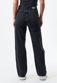 High-waisted black denim jeans with a straight leg cut, two back pockets, and a visible branded label at the waistband. Textured fabric.