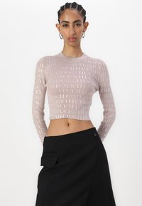 Rosa strikket crop-top med lange ermer, med gjentagende tekstmønster. Kombinert med høyt liv svarte bukser med sidelomme.