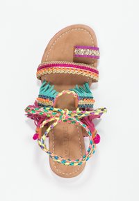 Sandale multicolore avec des sangles en tissu, présentant des accents tressés et à franges. Le matériau comprend du cuir avec des coutures décoratives et des embellissements.