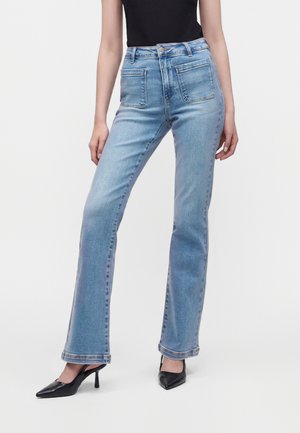 Kvinde iført lyseblå jeans med høj talje og lige ben med forlommer og sorte spidse hæle.