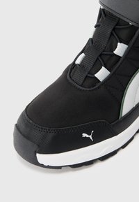 Svartvit Puma-sneaker med svart snörning, texturerad sula och vit Puma-logga på sidan nära framtill på skon.