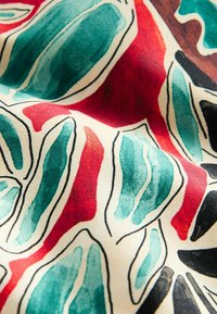 Látka s farebným abstraktným vzorom obsahujúcim tyrkysové, červené, čierne a hnedé tvary orámované čiernou farbou na svetlo béžovom pozadí.