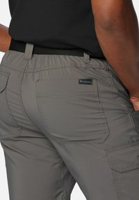 Gray cargo pants with elastic waistband, featuring multiple pockets and a fabric tag. Smooth texture and casual design suitable for outdoor use.