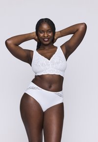 Bralette bianco in pizzo con bordi ondulati e slip hipster coordinati caratterizzati da pizzo decorativo, tessuto morbido e silhouette aderente.