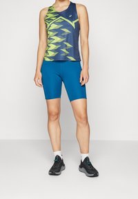 Modré sportovní šortky v kombinaci s bezrukávovým tank topem v námořnické modré a zelené s vzorem. Oblečení má těsný střih a je vyrobeno z materiálu odvádějícího vlhkost.