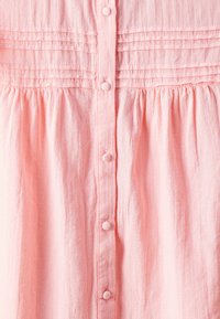 Camisa de botón rosa con pliegues horizontales en el pecho, textura fruncida y botones redondos en la parte delantera. Tejido suave y ligero.