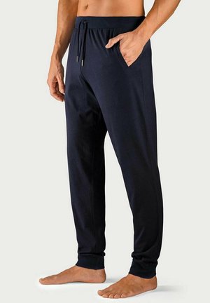 Man wearing navy blue jogger pants with elastic waistband and drawstring, standing barefoot with one hand in pocket.