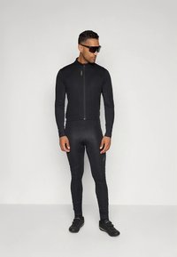 Zwart fietspak van rekbare stof, met een aansluitend ontwerp, volledige ritssluiting aan de voorkant en lange mouwen. Draagt zwarte fietsschoenen en een zonnebril.