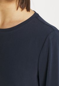 Marineblaue Rundhalsausschnitt-Oberteil mit langen Ärmeln, aus einem glatten, leichten Stoff gefertigt, mit einer subtilen Textur auf der Oberfläche.