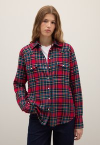 Red and blue plaid shirt in soft fabric, featuring a button-up front, two chest pockets, and a classic collar. Long sleeves with buttoned cuffs.